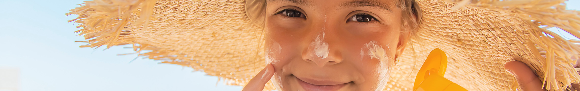 Child applying sunscreen to face while wearing large sun hat