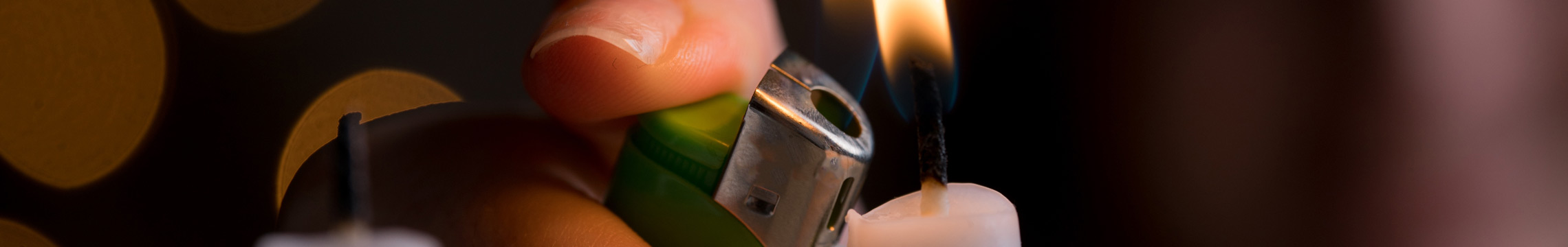 Close up of a hand using a green lighter to light a white candle