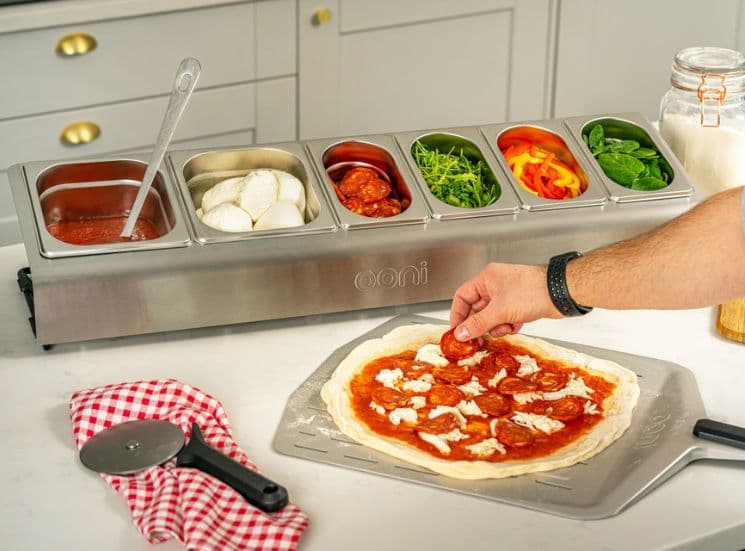 Adding toppings to a pizza from Ooni pizza topping station