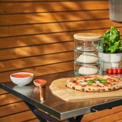 Ooni folding table holding pizza, spoon, sauce, dough, and toppings