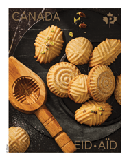 Stamp features photograph of nine maamoul on a dark serving tray and a carved wooden mould used to make them. Includes “Eid” and “Canada” text. 