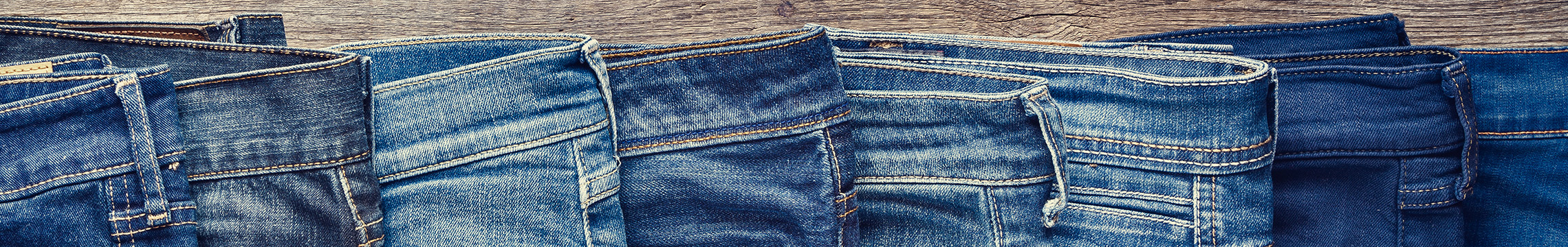Men's blue jeans fanned out across a wood table