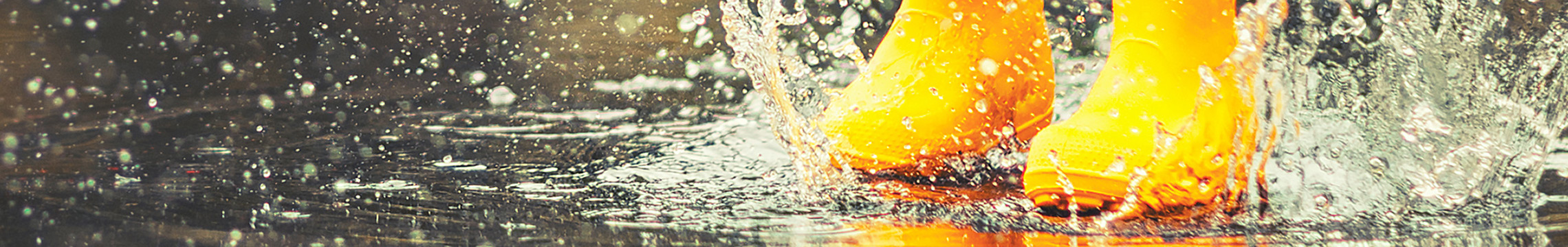 Child in yellow rainboots splashing in rain puddles