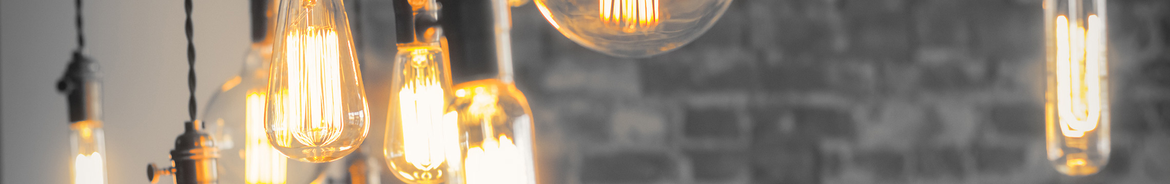 Vintage style Edison lightbulbs hanging from ceiling in front of grey brick wall