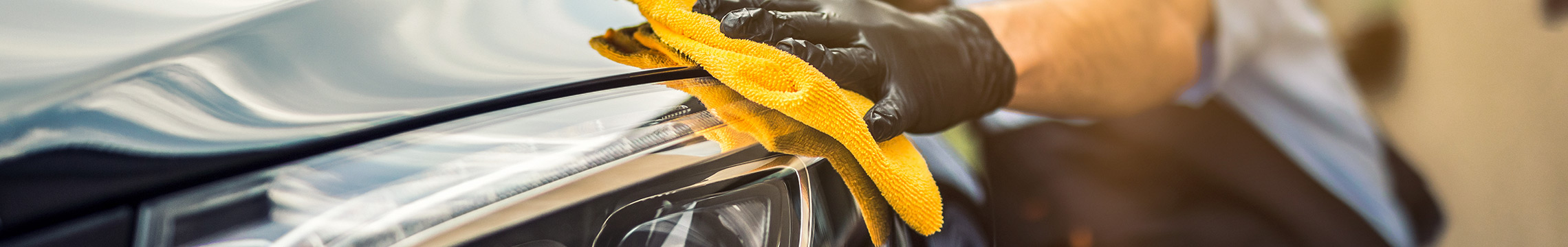 Man cleaning front car headlight with gloved hand