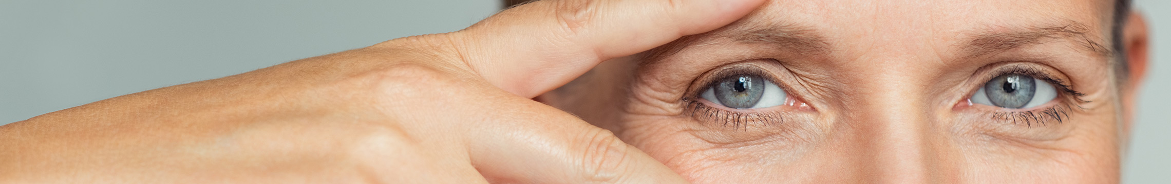 Woman framing her blue eyes with splayed fingers and smiling