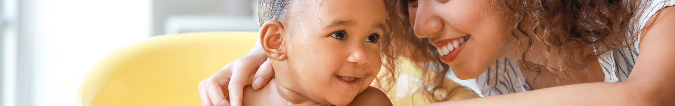 Baby in bathtub giggling while mother washes shoulders