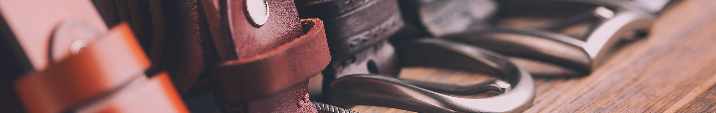 Variety of leather belts with metal buckles lined along a wooden shelf