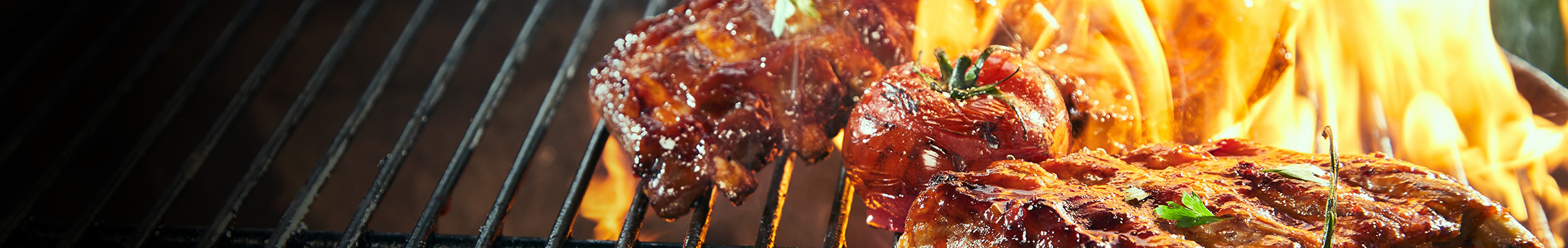 Flame-grilled meats and vegetables on an iron grill grate