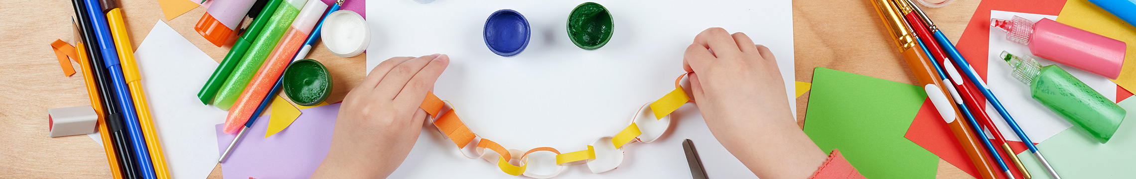 Child's hands string together a paper chain while surrounded by many craft supplies