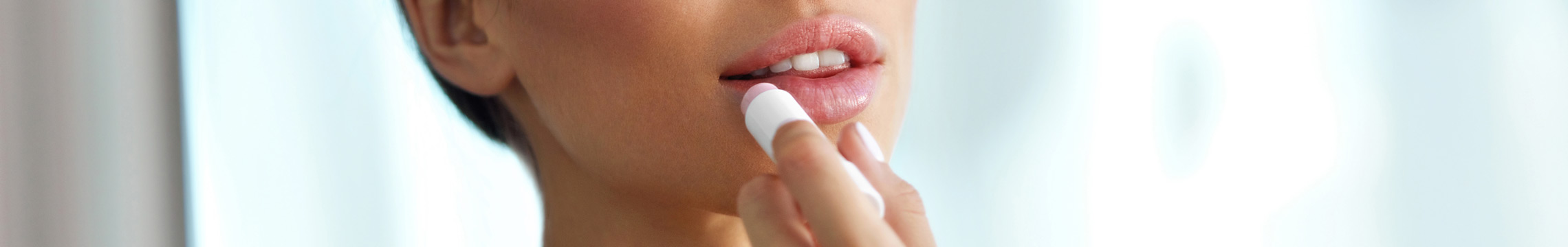 A young woman applies lip balm in a bathroom mirror