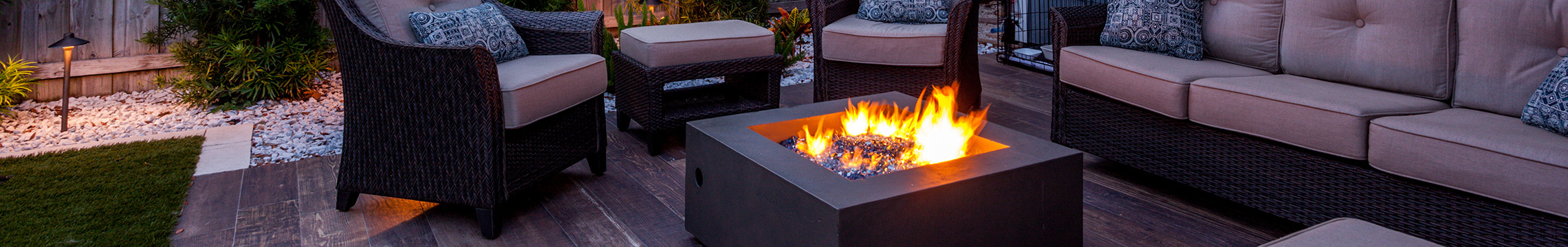 Outdoor lounge set circling a metal fire pit on a wooden deck at dusk