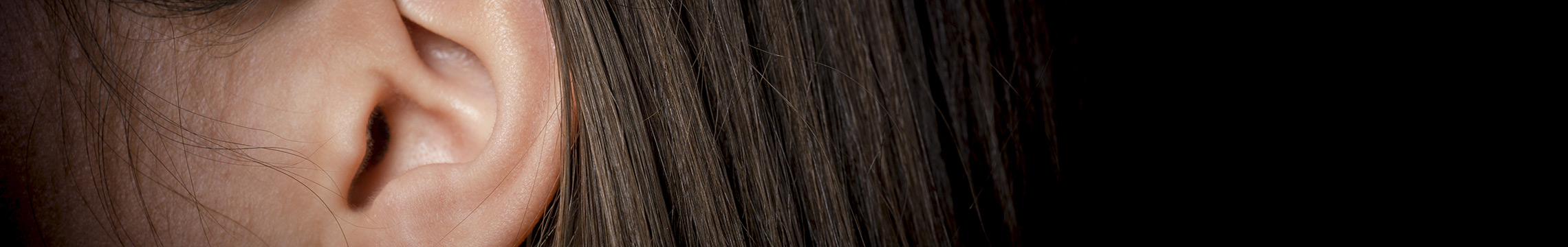 Close up of woman's ear surrounded by log, brunette hair