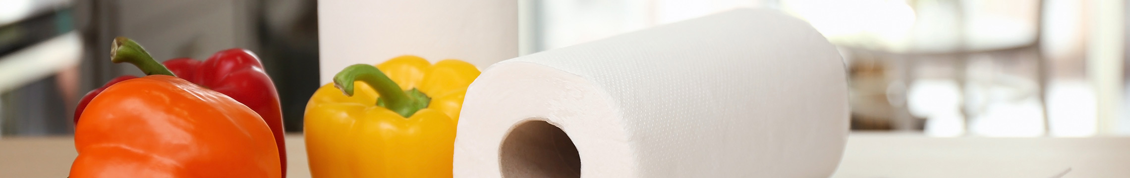 Paper towel rolls and colored bell peppers resting on a light wood counter in a brightly lit kitchen