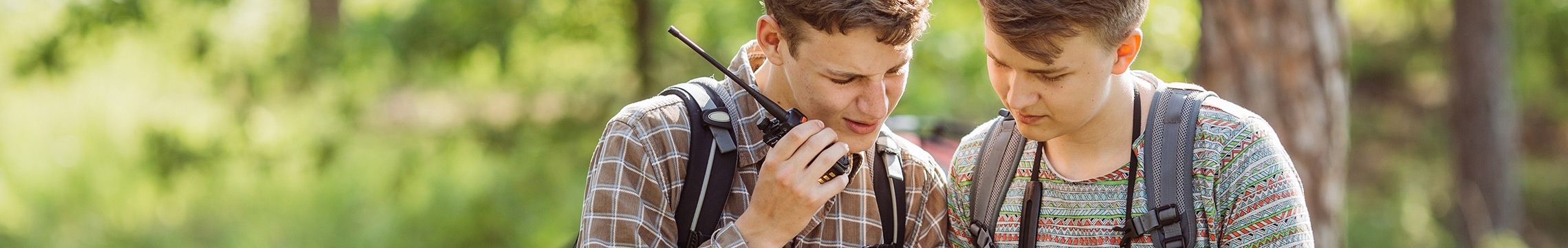 Two friends speaking into a walkie-talkie as they look at a map while camping