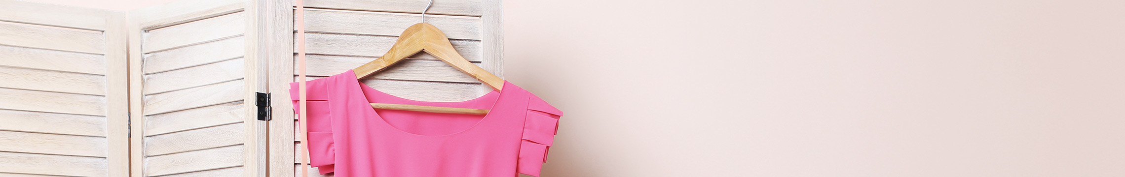 Pink dress hanging from a wooden hanger on a wood room divider