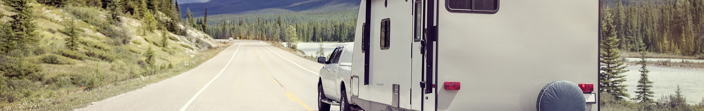 White travel trailer being towed through scenic landscape by white pickup truck