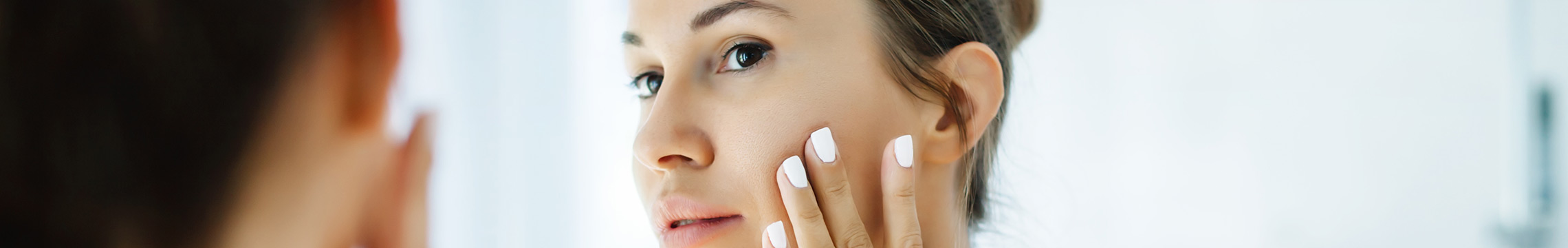 Women looking in a mirror, caressing her face, with hair pulled back
