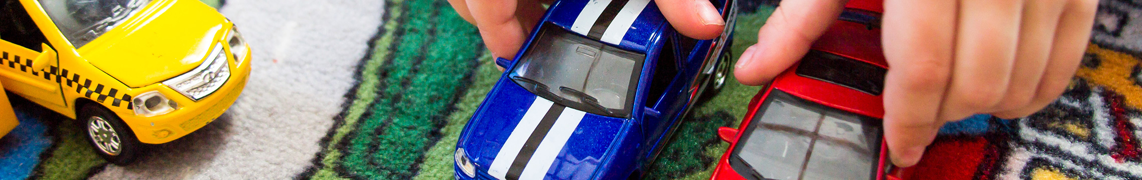 Close up of child's hands playing with red and blue toy cars