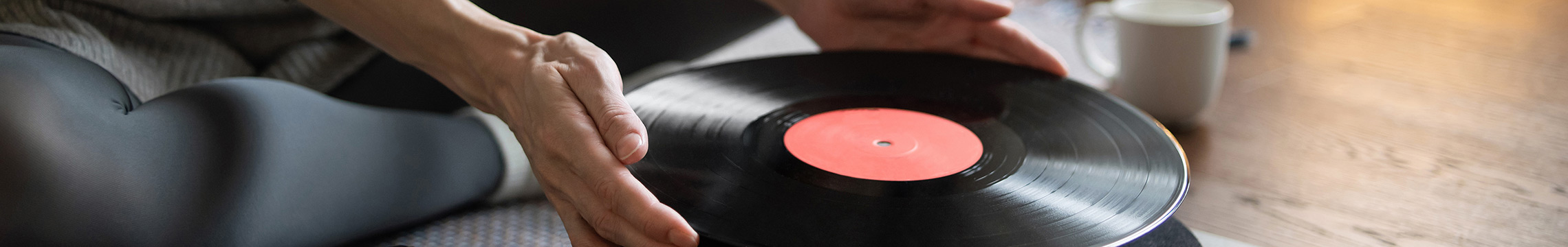 Woman placing vinyl record on record player while sitting on living room floor