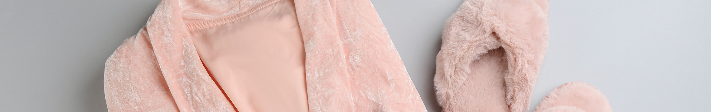 Woman's soft pink robe with matching slippers and satin face mask against a grey background