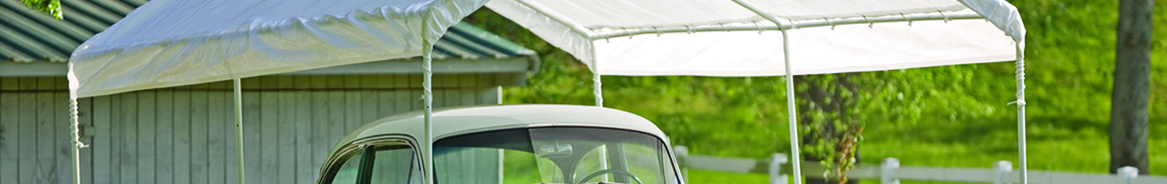 Green vintage car parked beneath white shelter canopy in grassy field