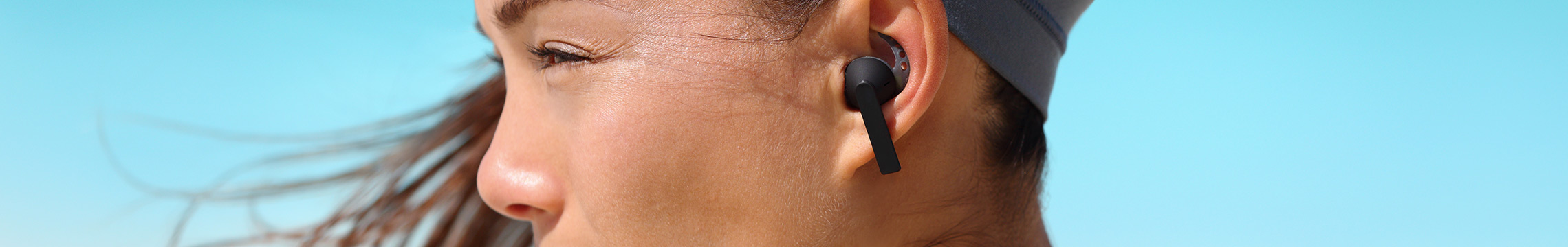 Woman on beach listening to wireless headphones while staring at something in the distance