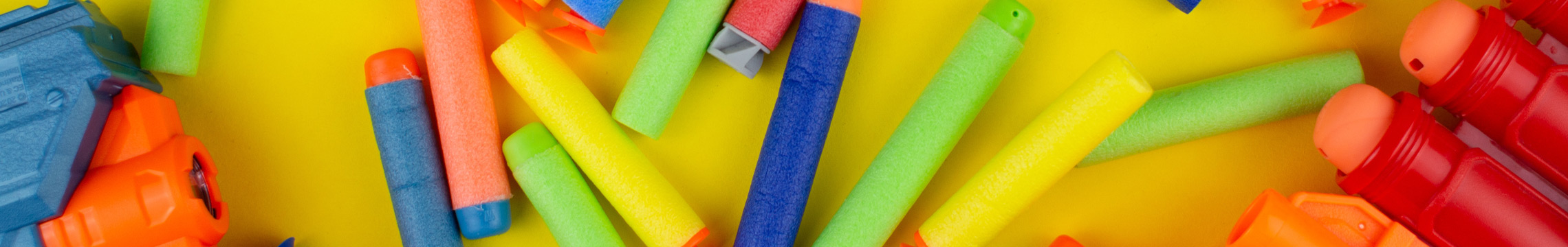 Many foam darts & dart guns laying against a yellow background