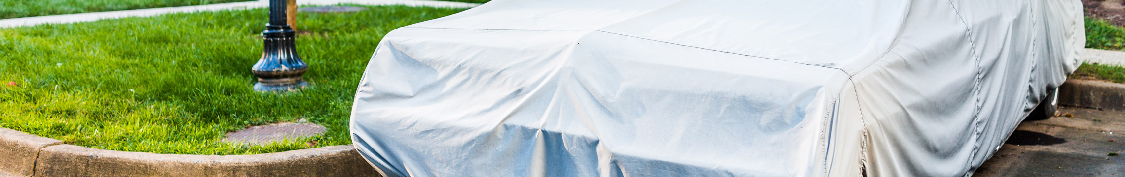 A car completely obscured by a grey car cover is parked in front of a row of suburban houses