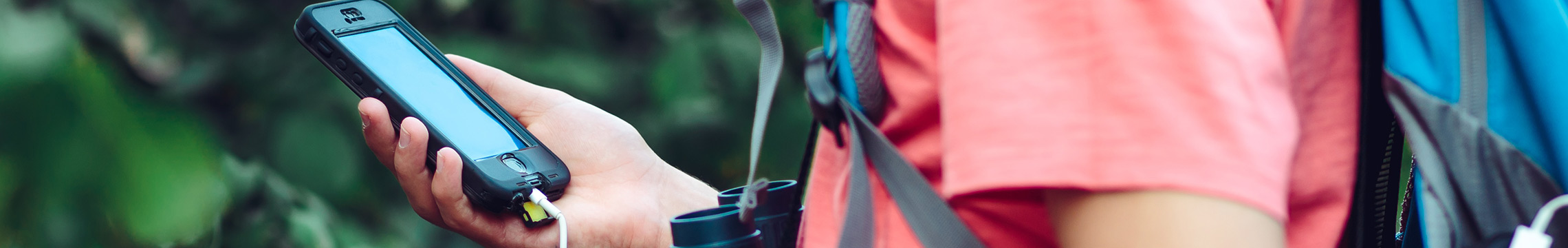 Man charging cell phone via portable charger while on a hiking trip