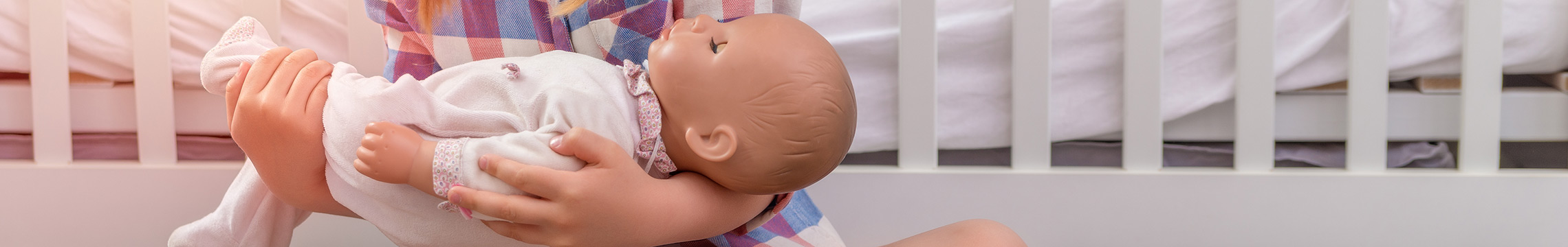 Little girl rocks a baby doll to sleep while sitting on her bedroom floor