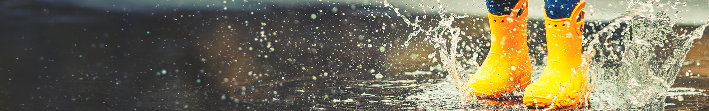 Bright yellow children's rain boots splashing in a puddle