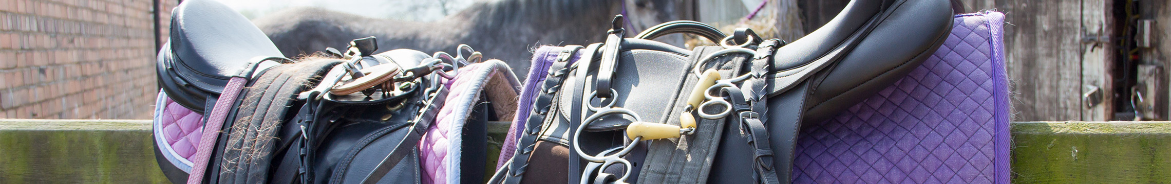 Saddles and blankets sitting on a fence in the sun