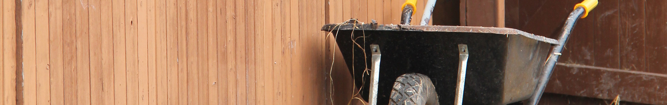 Black wheelbarrow parked outside a brown equine barn